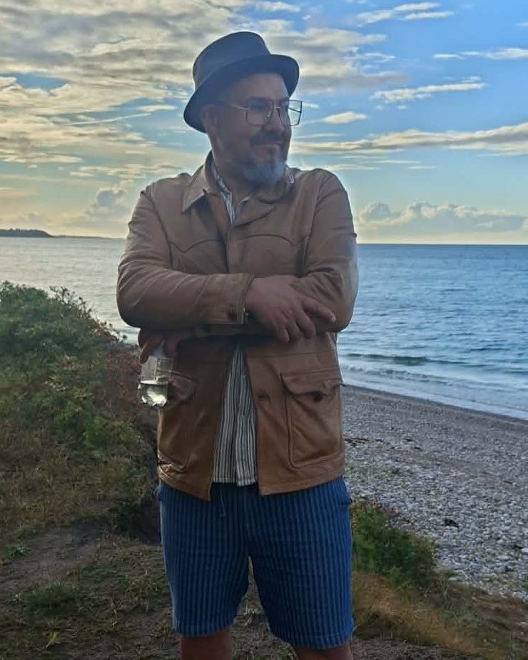 Steven Wensley ved stranden, i læderjakke og hat.