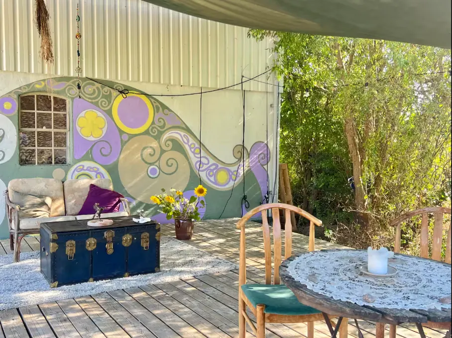 Overdækket terrasse med bord, stole og en bemalet væg.