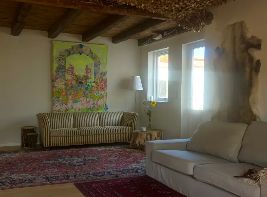 Salen med sofa, tæppe og maleri under skråt træloft.