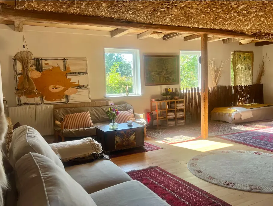 Salen med sofaer og tæpper under et loft af tang og synlige bjælker.